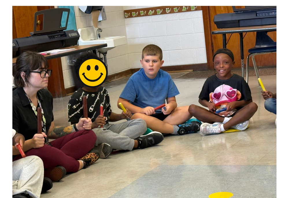 Students sit in a circle playing rhythm sticks during a back-to-school music class.