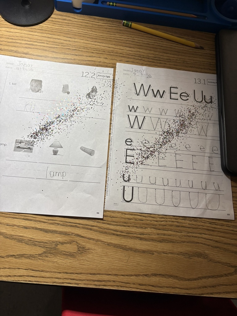 Two completed handwriting worksheets on a desk, sprinkled with fairy dust to celebrate great work.