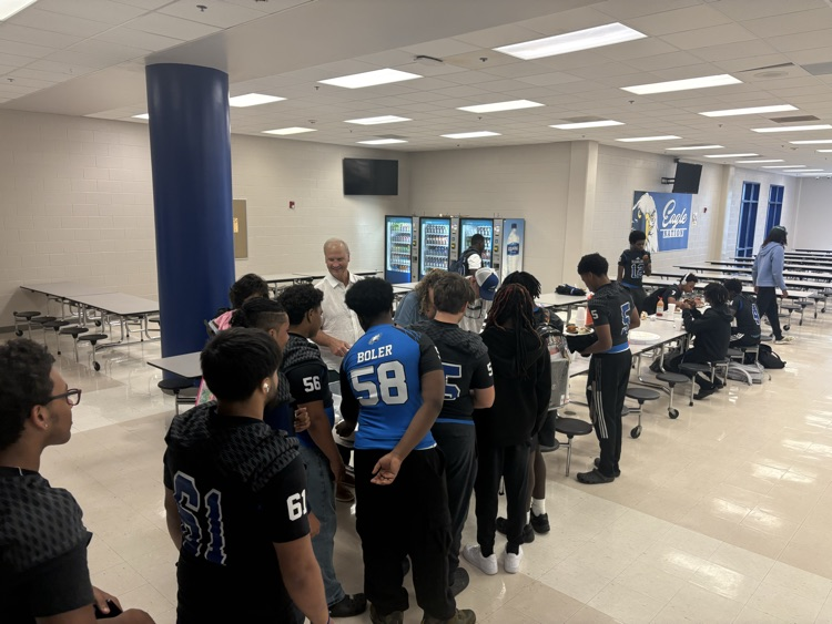 several football players stand in line as they wait for their pregame meal while a couple people serve them