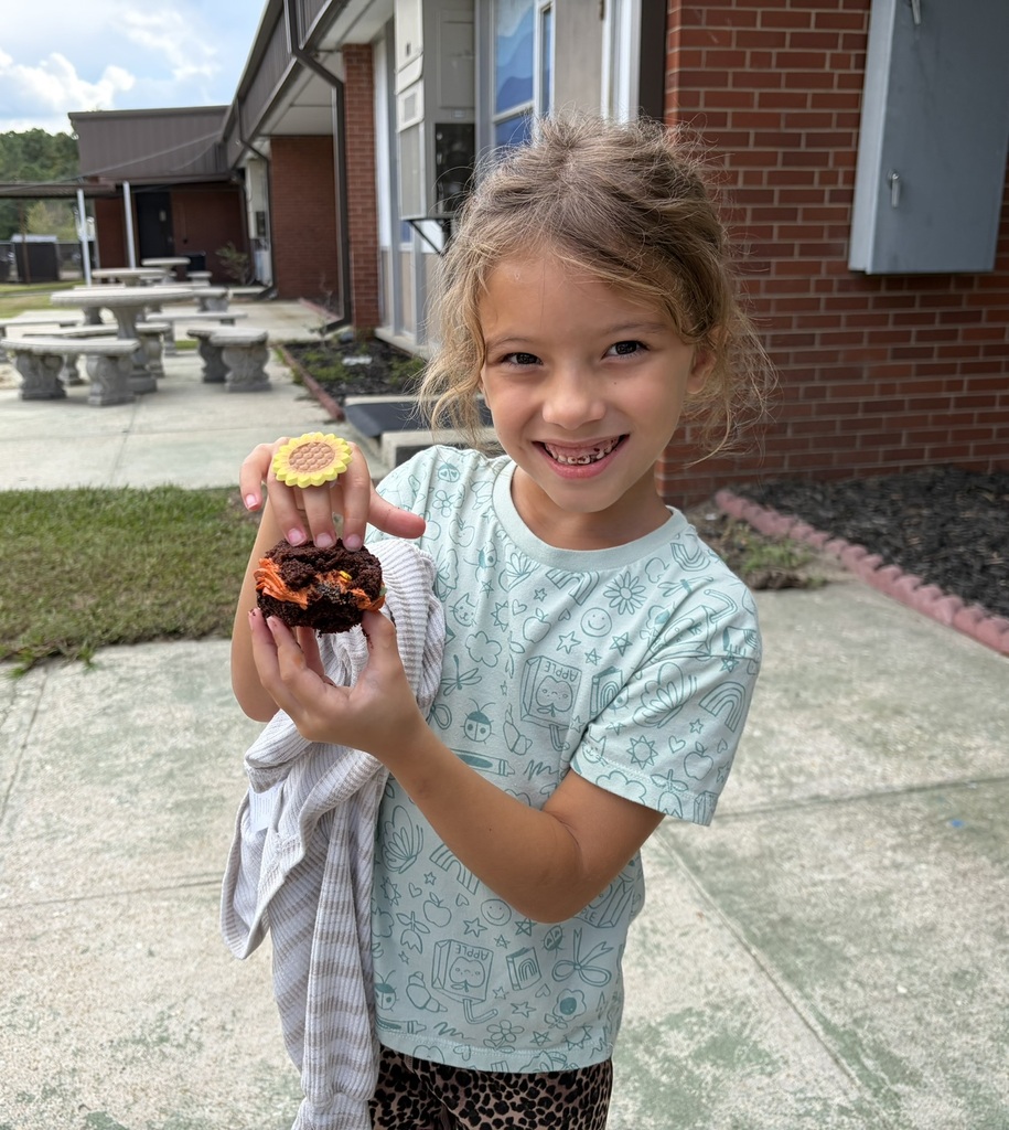 a smiling student holds her cupcake outside.