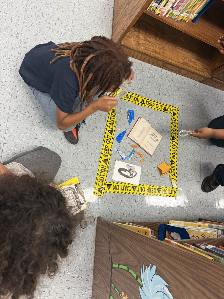 Students use magnifying glasses to investigate clues at a library book “crime scene.”