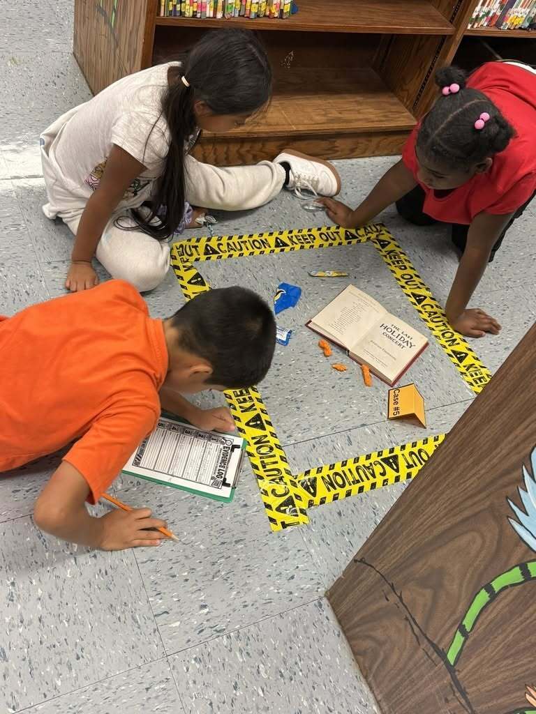 Three elementary students look at a fake library crime scene .