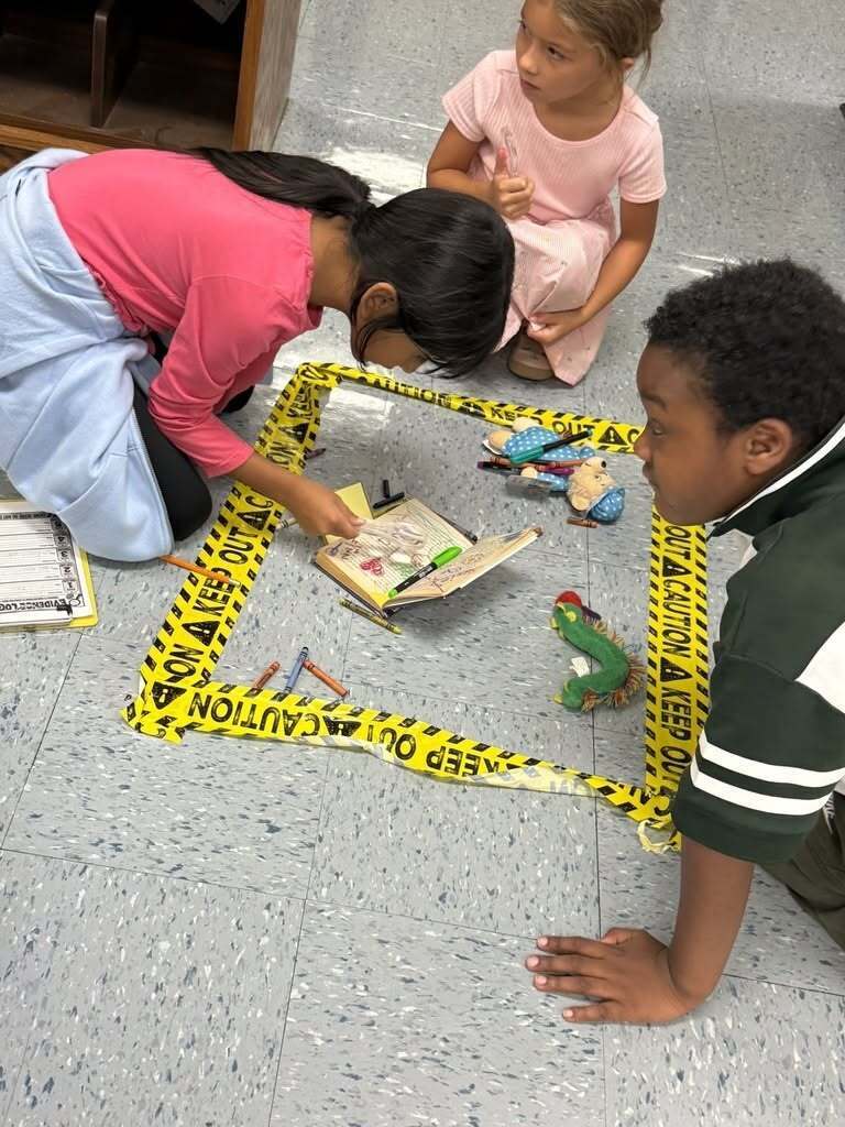 Students are investigating a fake library crime scene set up on the floor.