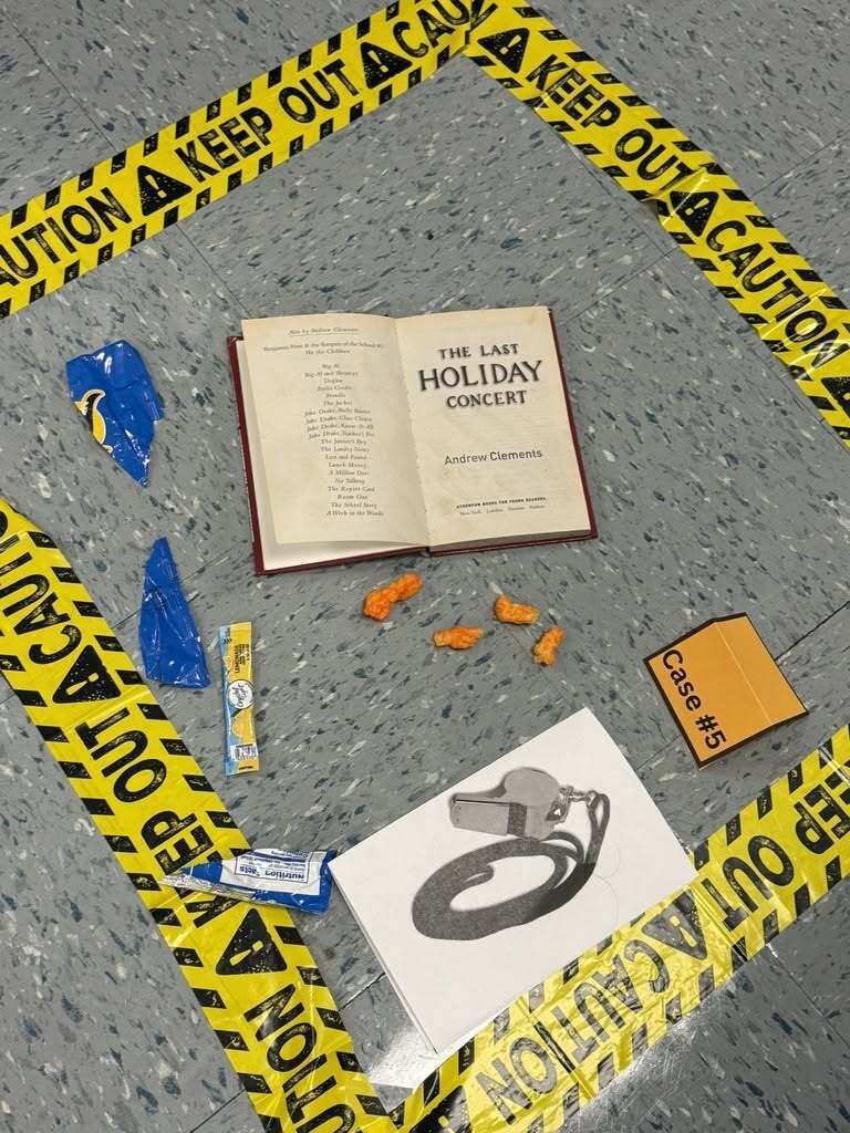 On the floor there is a square of caution keep out tape. Within the scare is an open book, a photo of a whistle, and bits of blue and orange.