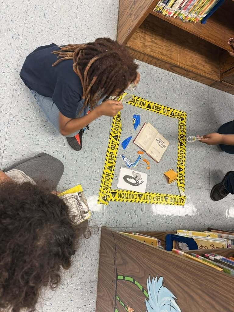 Students are investigating a library fake crime scene on the floor.
