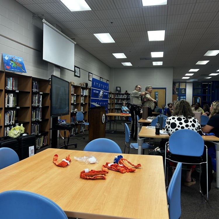 two officer stand in front of a group of teachers in a library as a show how to apply a tourniquet