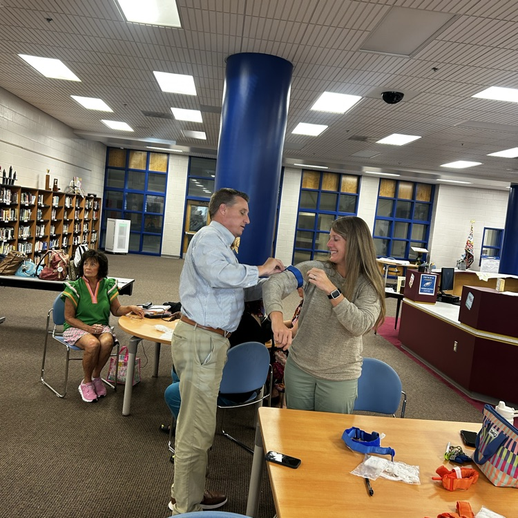 A female teacher applies a tourniquet to a male teacher as they get tested during a presentation in the library