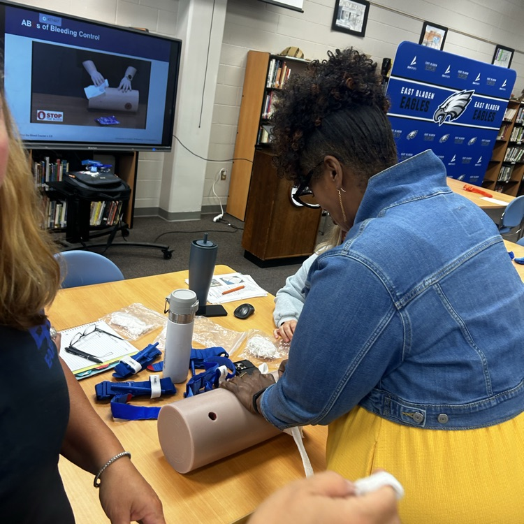 A lady in a yellow dress and jean jacket applies pressure to a mannequin