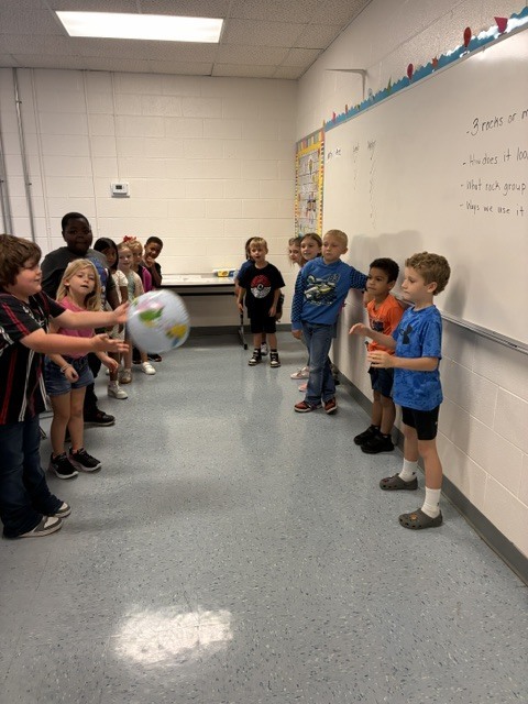 students tossing an inflatable globe to each other using right thumb as an indicator,