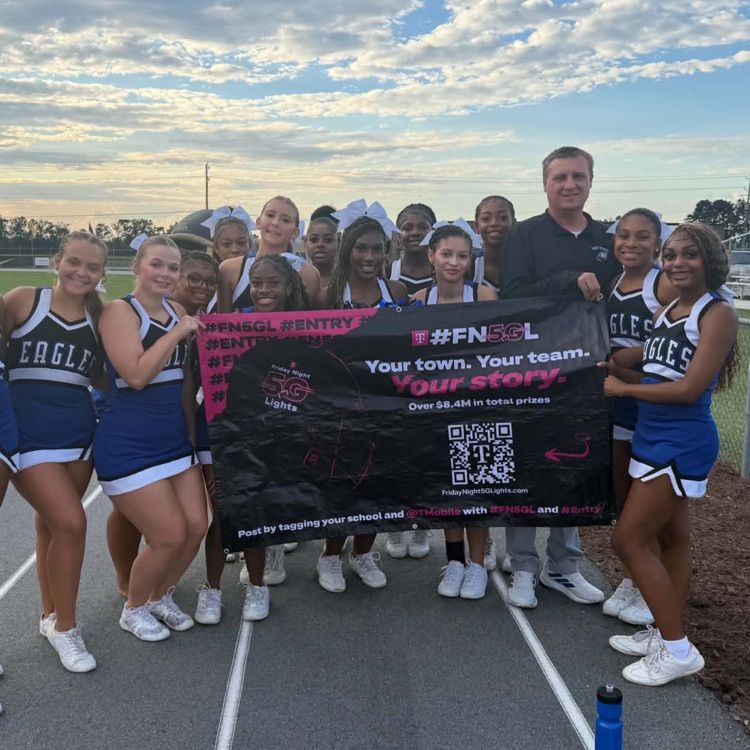 cheerleaders and blue white and black uniforms stand with Principal on track holding a black and pink banner for T-Mobile