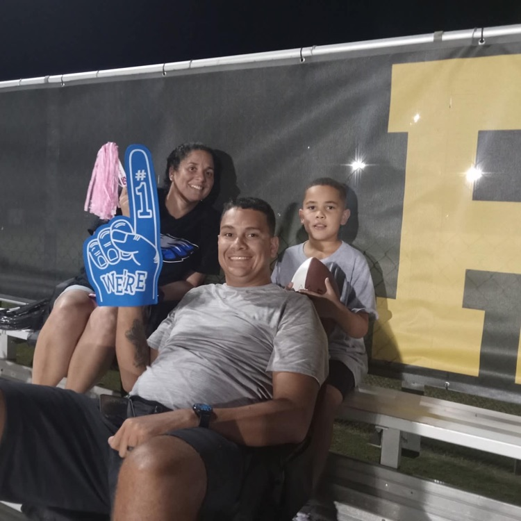 Man and woman and young child pose at football game with foam fingers and pink pom-poms to show school spirit