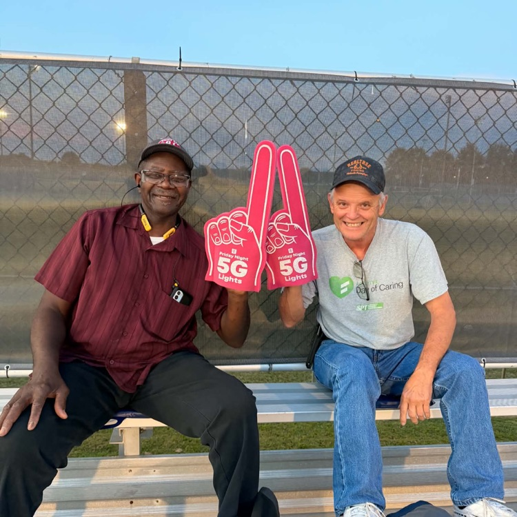 Man and Burgundy shirt, black pants and men and white shirt, jeans pose with pink 5G, T-Mobile foam fingers