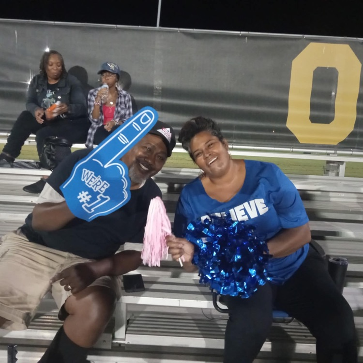 men in black shirt, khaki shorts, women and eagle blue shirt, and black pants posed with blue pom-poms and foam fingers