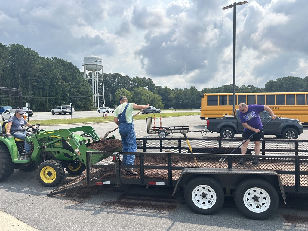 People scooping soil from a trailer into a tractor bucket.