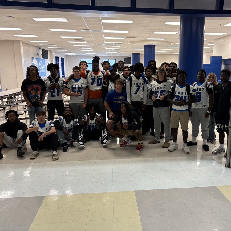 Group of football player, standing in some sitting on the cafeteria floor as they pose in their jerseys before the football game