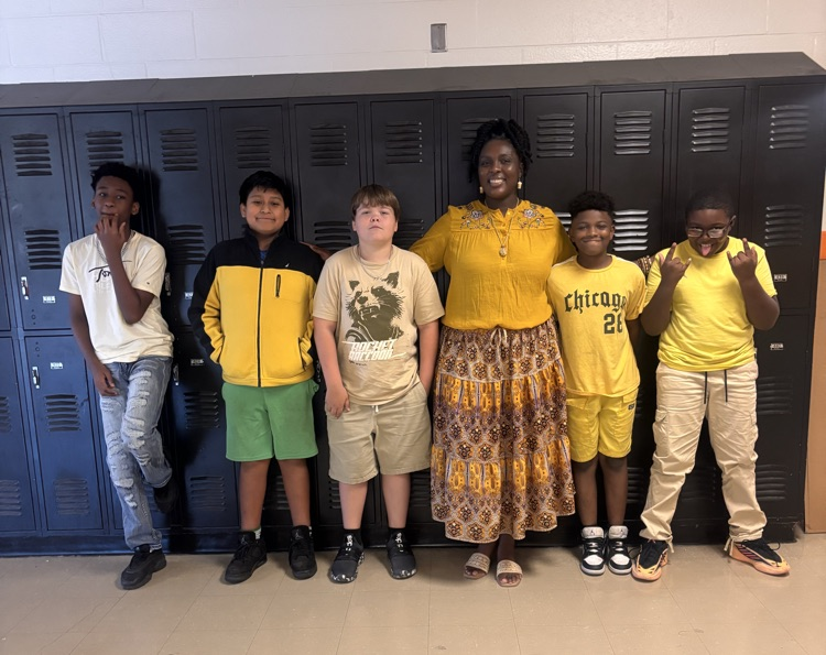 Students and teacher smiling in hallway in front of lockers.