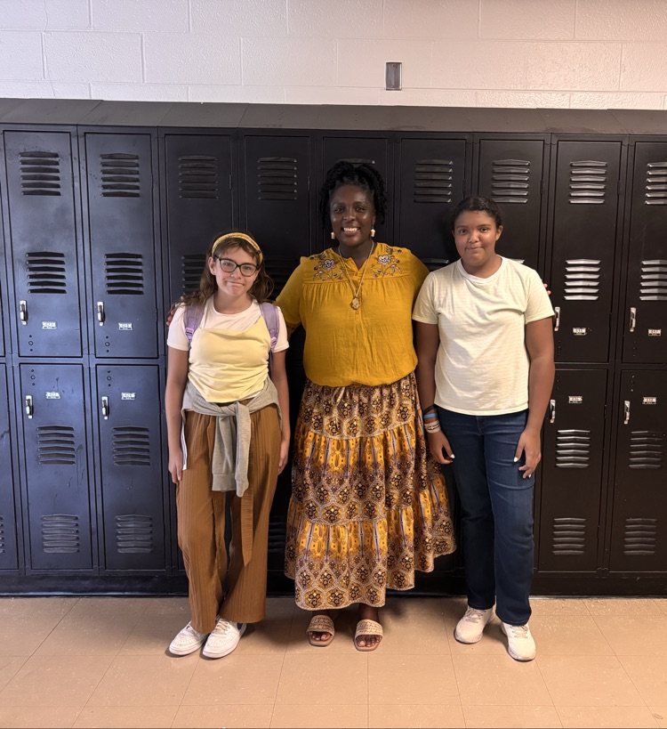 Students and teacher smiling in hallway in front of lockers.