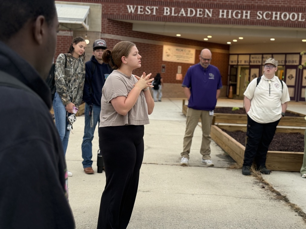 A student addresses a group of peers and staff gathered outside West Bladen High School near the entrance