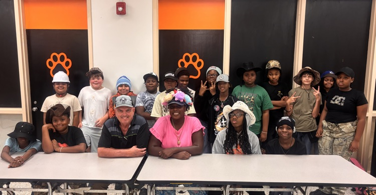 teachers and students in cafeteria sitting at a table, and students in a line behind them.