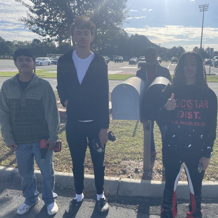 three guys and a teacher standing beside a mailbox