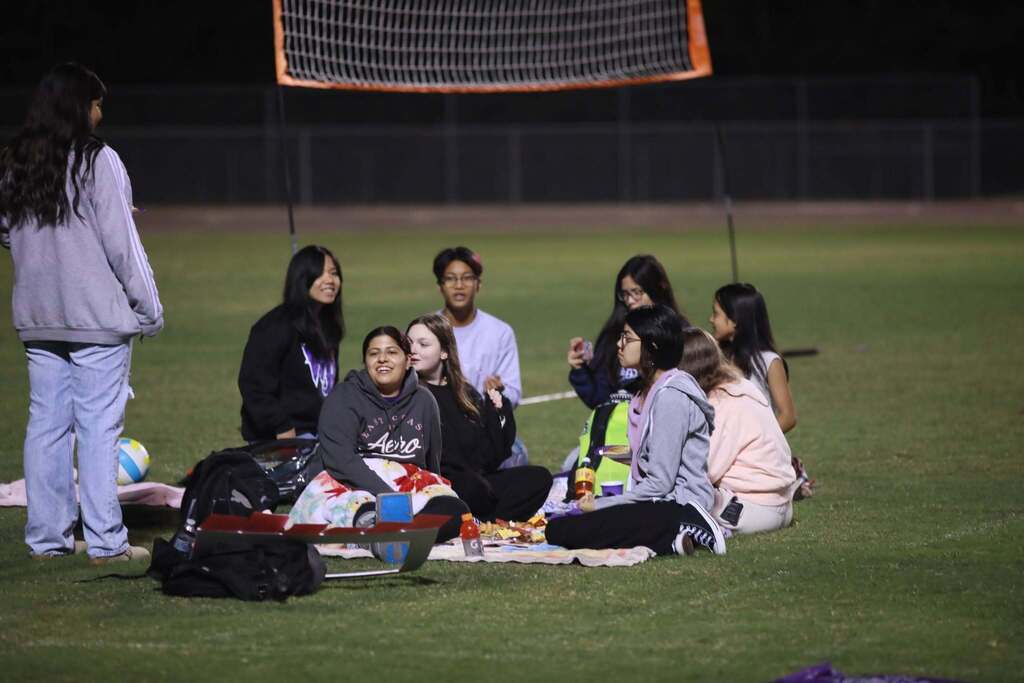 Students sit together on blankets on a grassy field at night during an early morning Senior Sunrise event.