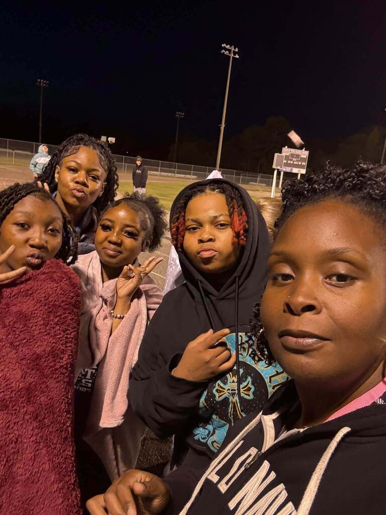 A group of smiling students pose for a close-up selfie at night on a football field during Senior Sunrise.