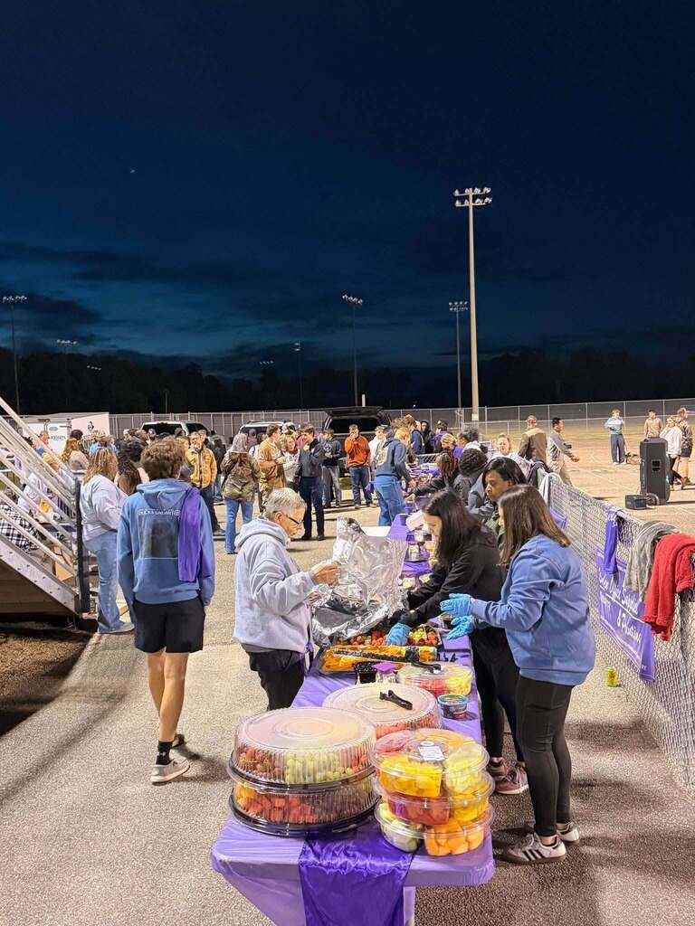 People set up breakfast trays on long tables decorated in purple during an early morning Senior Sunrise event.