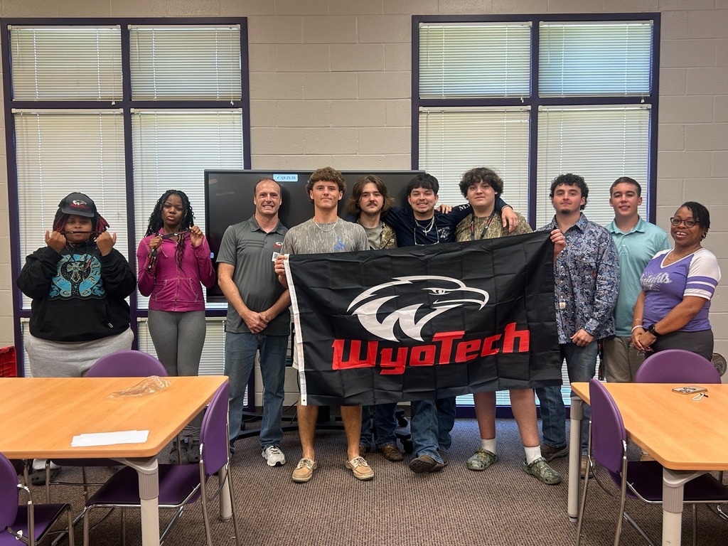Students, staff, and a WyoTech representative pose together after the information session while holding a large WyoTech flag.