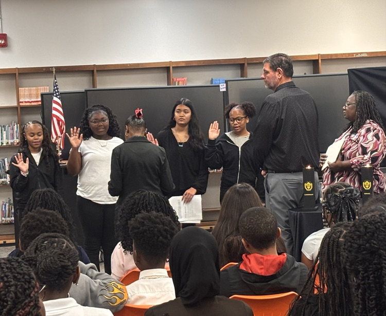 student right hand up making beta pledge at ceremony in front of sponsors and principal