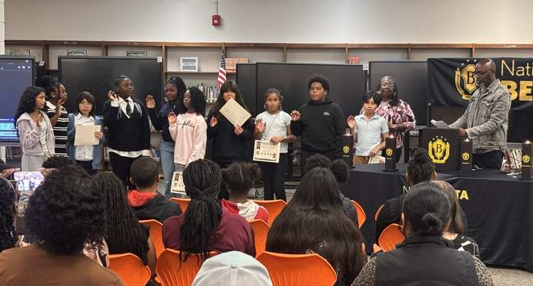 new inductees right hand up saying beta pledge in front of audience, principal, and sponsors