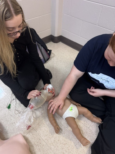 Students practice infant CPR and bag valve mask ventilation on a training mannequin.