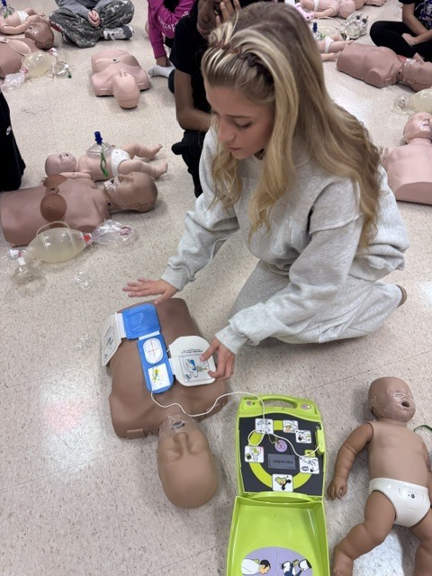 A student practices CPR on an infant training mannequin in a classroom setting