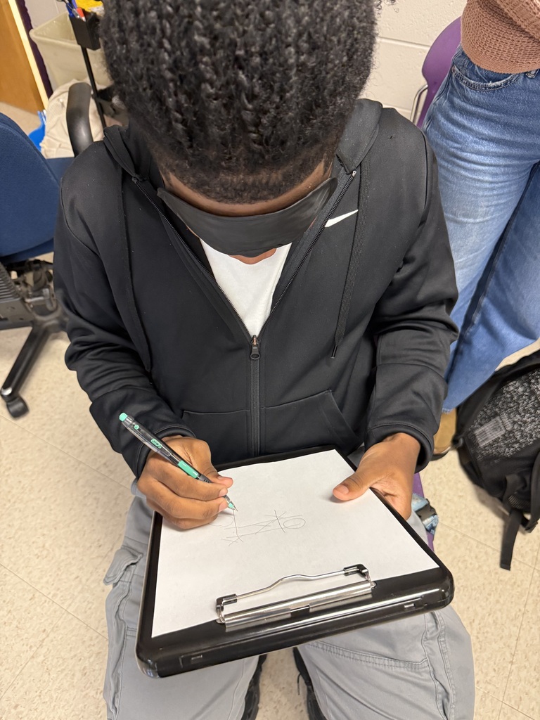 A close-up of a blindfolded student sitting down while drawing or writing on paper during a classroom activity
