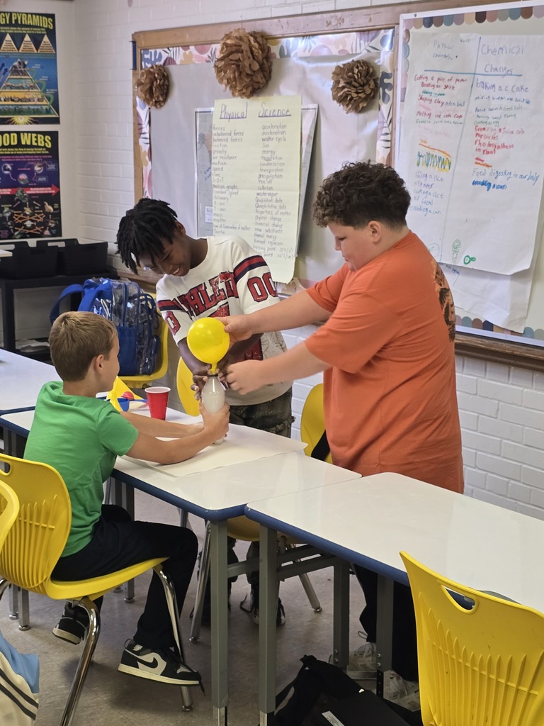Bladenboro Middle School fifth graders observe a yellow balloon inflated during their chemical reaction lab. One student holds the bottle while another examines the results, demonstrating teamwork and exploring how chemical reactions produce gas and cause observable changes in matter.