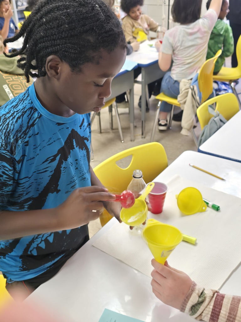 Bladenboro Middle School fifth grader carefully measures a substance into a yellow funnel during a hands-on chemical reaction lab. Working with classmates, the student prepares materials for an experiment exploring how combining substances can produce gas and demonstrate changes in matter.
