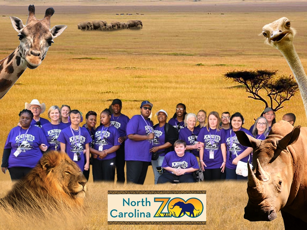 Group of students and chaperones in purple shirts at the zoo with a prairie background with lion and rhino
