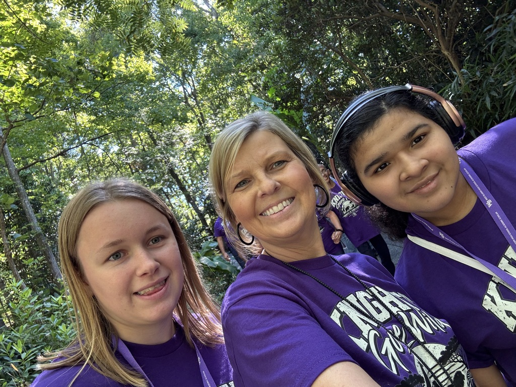 Teacher and two female students all in purple shirts posing as they explore the NC zoo