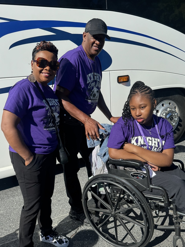 Student is in purple shirt and in a wheelchair being pushed by her grandfather who is is also in a purple shirt along with a lady in a purple shirt beside her