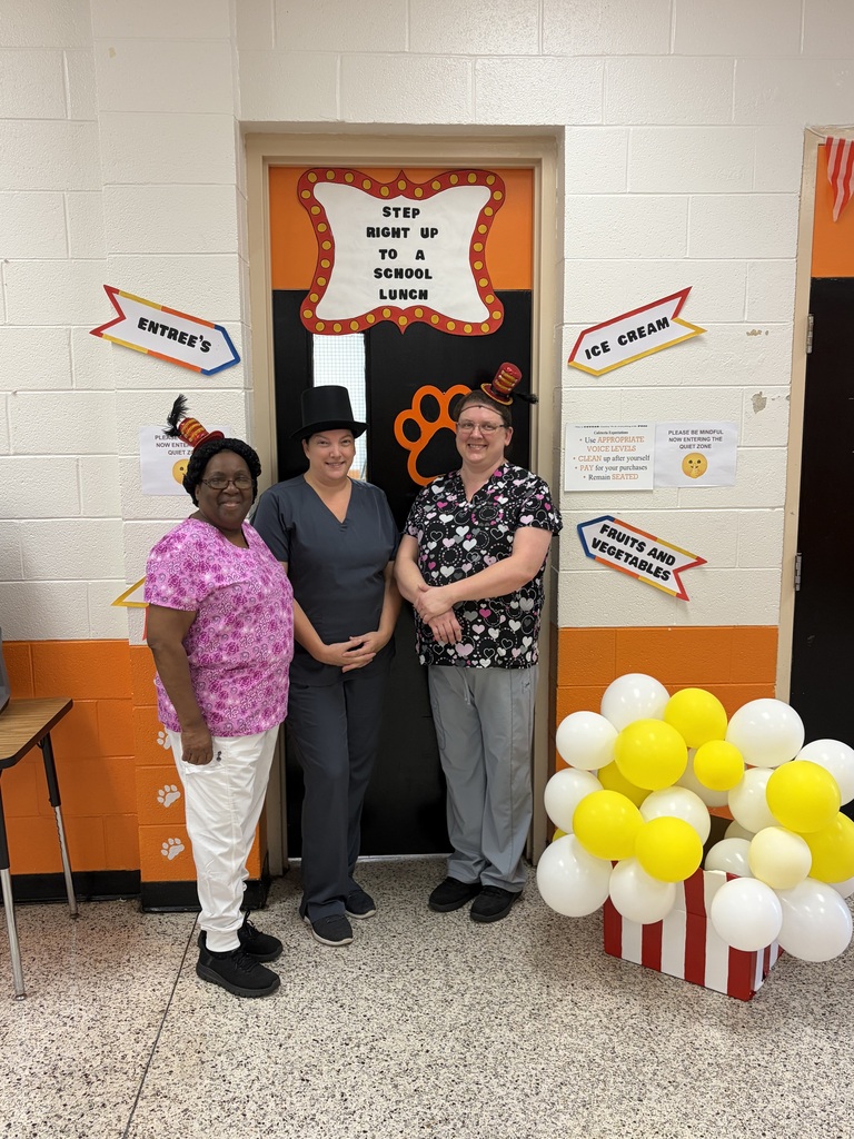 Three cafeteria staff members stand smiling with circus themed props.