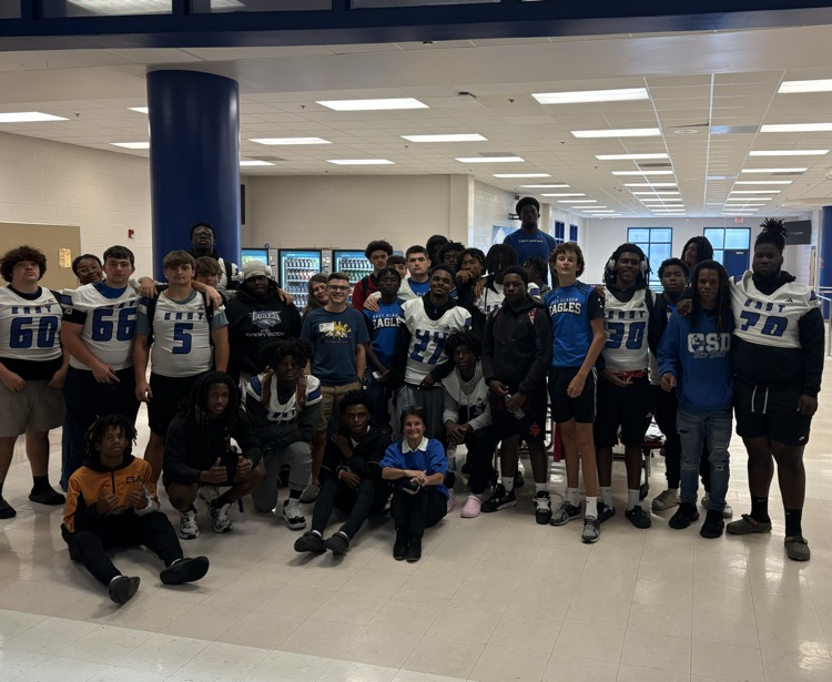 group of football players standing and some sitting on the floor with assistant principal Mrs. Owens-Ross and a couple church representatives stand in the back  