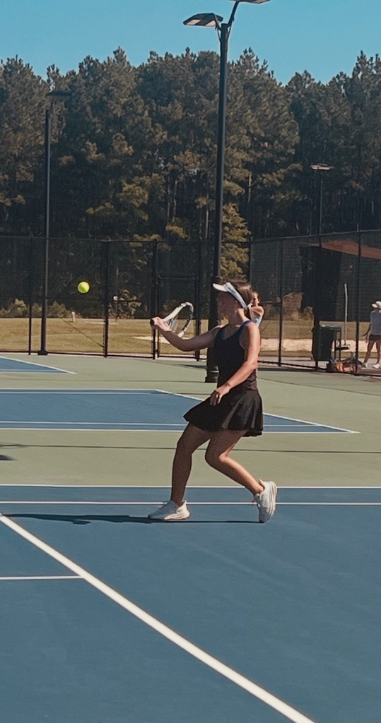 student in black tennis skirt on a tennis court heading to hit a tennis ball