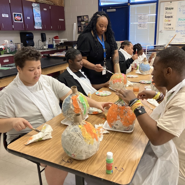 three students and a teacher working on painting, papier-mâché pumpkins