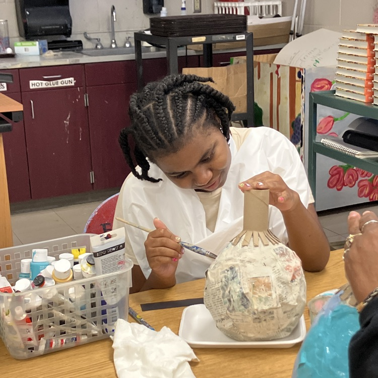 student working carefully to paint her papier-mâché pumpkin