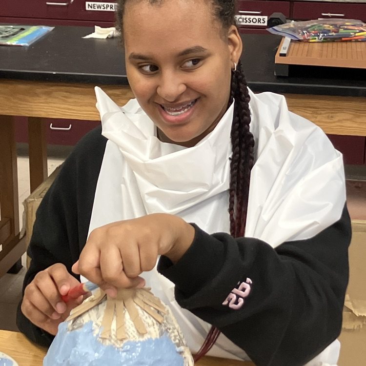 students seem smiling as she paints her pumpkin