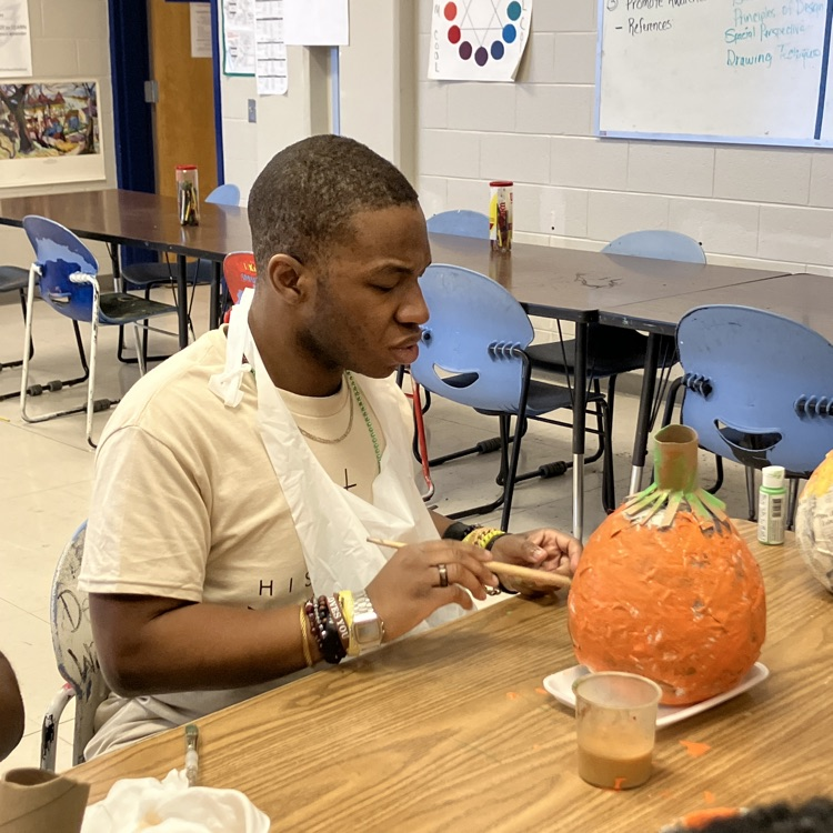 A student paint a pumpkin out of papier-mâché
