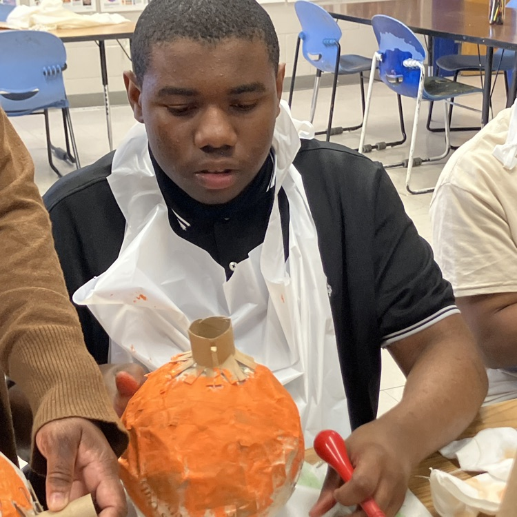 A student paint, a papier-mâché pumpkin orange in art class