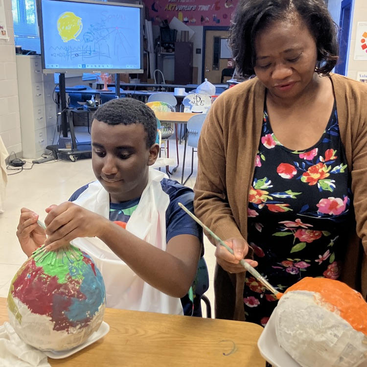 A teacher and student painting paper, Mâché pumpkins in a art class
