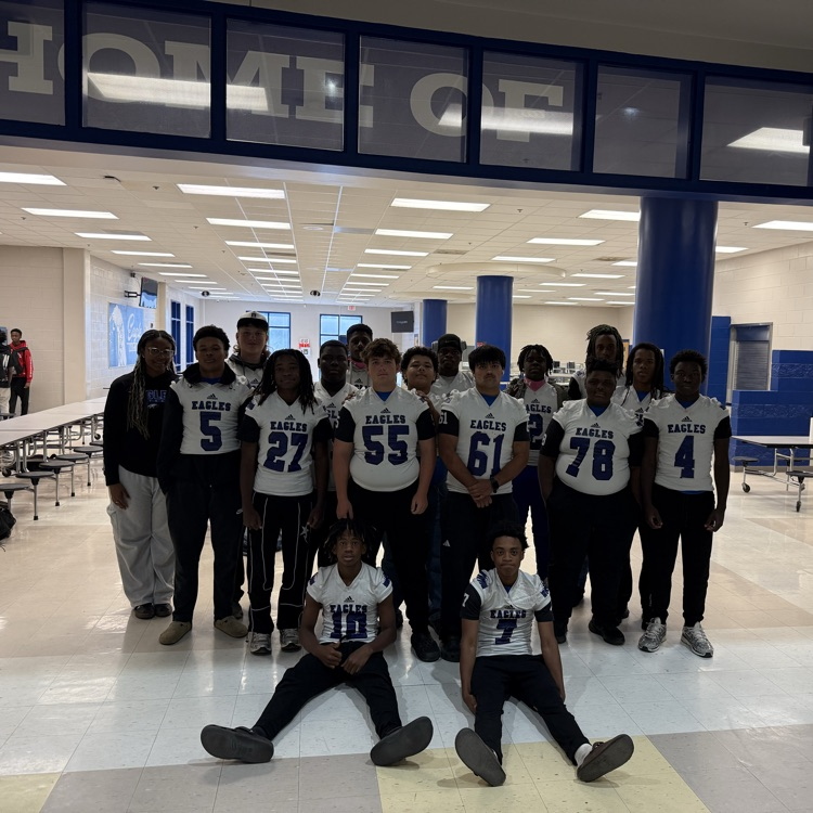 football team in white jerseys with blue numbers standing and seating posing in front of a cafeteria