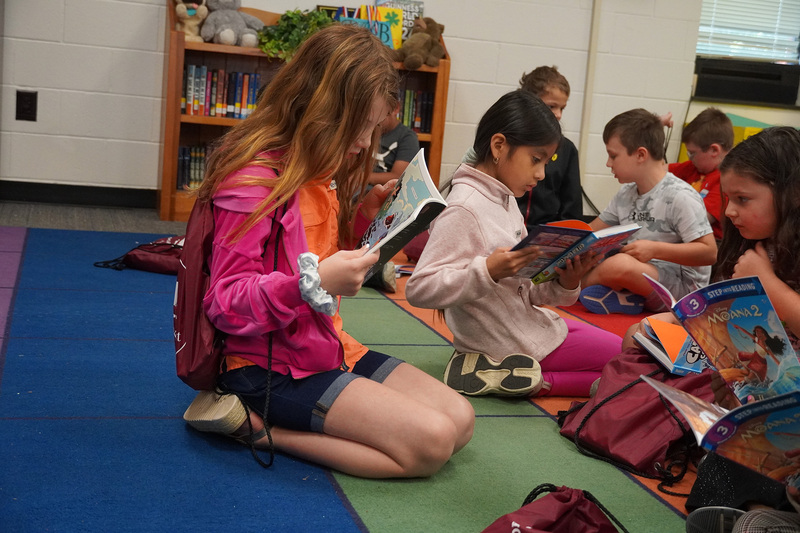 A group of elementary students sit on the carpet reading books.
