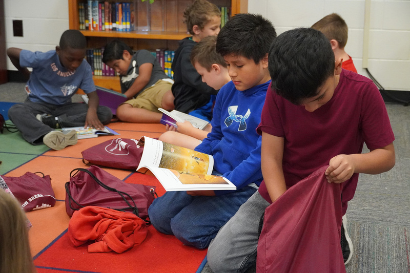Students sit together on the carpet looking at new books.